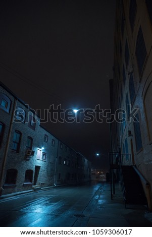 Dark foggy urban city alley at night after a rain with vintage warehouses