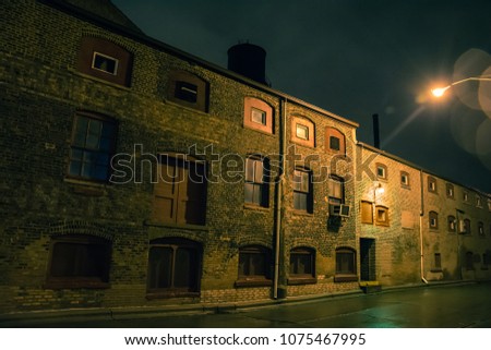 Dark urban city alley at night after a rain featuring vintage warehouses