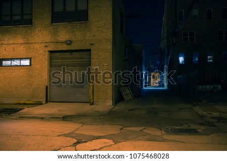 Dark city street corner and alley with an industrial building entrance at night