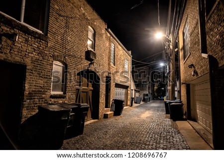 Dark and eerie urban city cobblestone brick paved alley at night