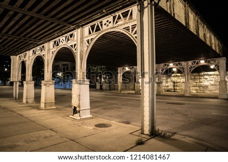 City street sidewalk and alley at night under a vintage train bridge