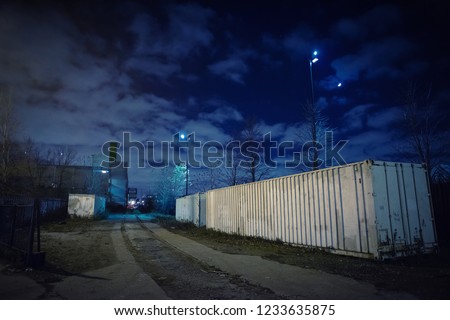 Eerie industrial urban street city night scene with truck cargo freight shipping containers, train railroad tracks, vintage factory warehouses, and the moon.