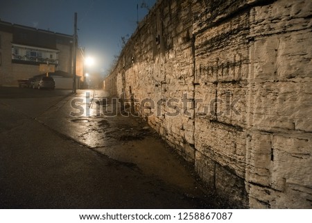 City street sidewalk and alley next to a vintage railway bridge wall at night