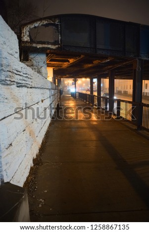 Scary city street sidewalk at night under a vintage train bridge