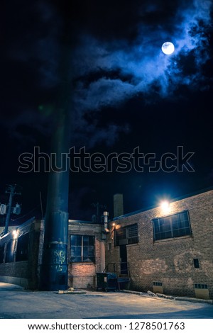 Dark and eerie urban city alley with vintage warehouses factory buildings and the moon at night in Chicago