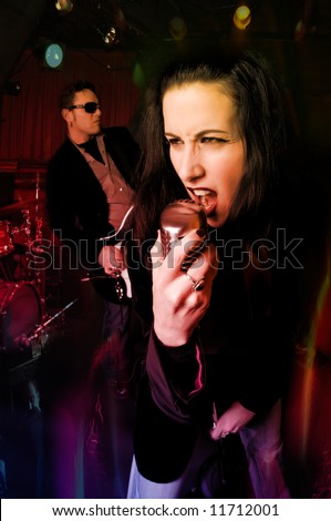 Close-up of female lead singer with retro mic and music band in background