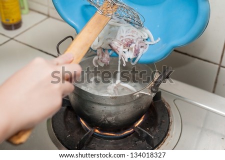a hand pouring fresh squid in the hot water
