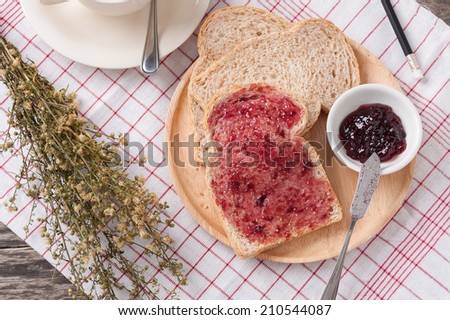 Sliced hole wheat bread with blueberry jam and a cup of coffee in wood dish on table.