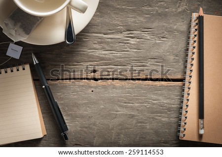 Small notepad with empty coffee cup, tea bag, pen and pencil on rustic wood background with low key scene