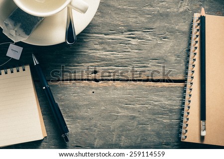 Small notepad with empty coffee cup, tea bag, pen and pencil on rustic wood background with film filter effect