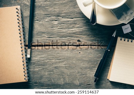 Small notepad with empty coffee cup, tea bag, pen and pencil on rustic wood background with film filter effect