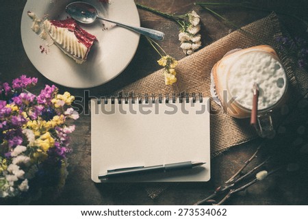 Notepad with pen, a glass of Thai tea and bits of red velvet cake on rustic wood background with film filter effect