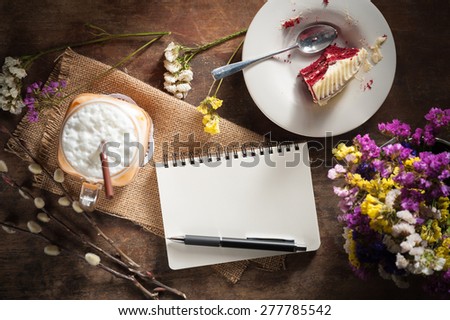 Notepad with pen, a glass of Thai tea and bits of red velvet cake on rustic wood background with low key scene