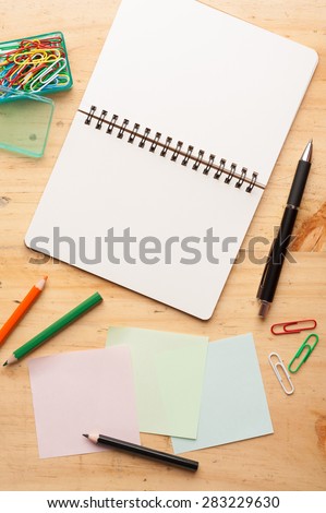 Notebook and sticky paper, paper clip, color pencil, and pen on wood table