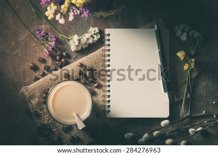 Notepad with pen, a glass of Thai tea on rustic wood background with film filter effect