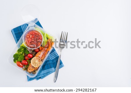 Grilled salmon with tomato salsa and salad cooked by clean food concept in lunch box on white table