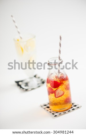 Iced strawberry tea in glass bottle with striped straw with iced lemonade in background