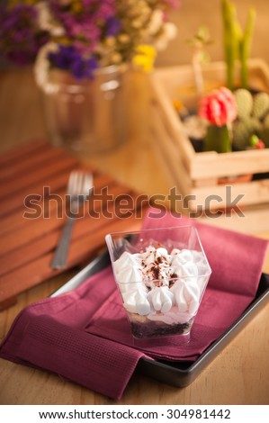 Banoffee pie in plastic cup on red napkin in black dish on wood table with afternoon scene