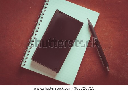 Opened notepad with pen and black smart phone on rustic cement background with film filter effect