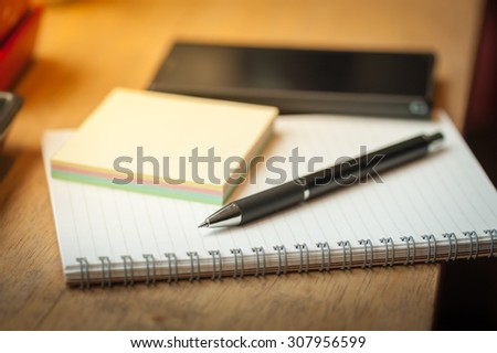 Opened notepad with pen, small sticky paper and black smart phone on wood bar in coffee shop in morning scene