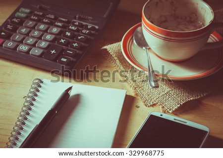 Opened notepad, pen, smart phone, and calculator on wood table in evening time with low key scene and film filter effect