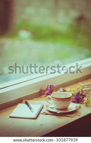 Coffee cup, opened notebook, and pen on wood bar beside window at coffee shop in afternoon time