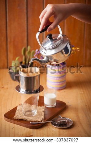 Woman right hand pouring hot water into Vietnamese style coffee dripper above empty vintage glass to make Thai tea in cafe