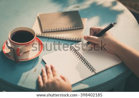 Woman right hand writing journal on small notebook at outdoor area in cafe with morning scene and vintage filter effect
