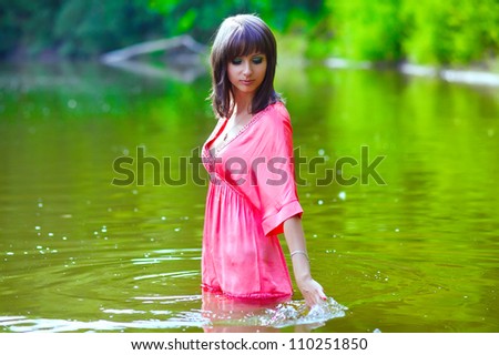 brunette woman in a red dress is wet to the waist in the water touches the hand of the river