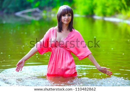 brunette woman in a red dress is wet to waist in water touches hand of river