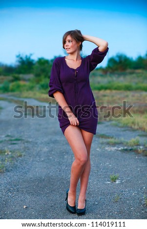 young woman knitted dress of purple on blue background with natural breasts and shoulders bare feet in black shoes