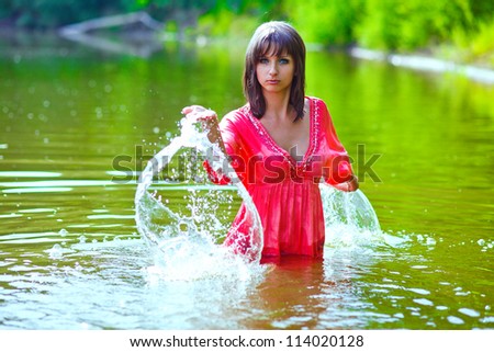 brunette woman red dress is wet to waist in splash water touches hand of river