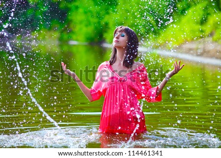 woman model in a red dress is standing in the rain to the waist in water on a green background in the street