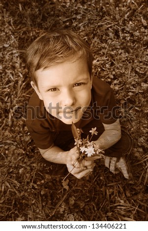 Retro black and white photo of sepia Boy sitting on green grass in spring and keeps the flowers snowdrops