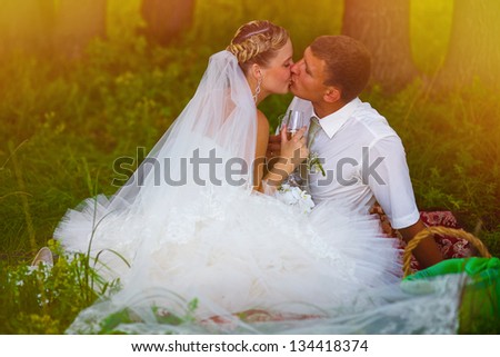 sunlight bride and groom at wedding in green forest sitting on picnic, drink from wine glasses at wedding