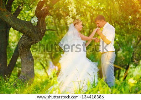 sunlight bride groom kissing hand of blonde bride, newlyweds couple are in green forest in wedding summer