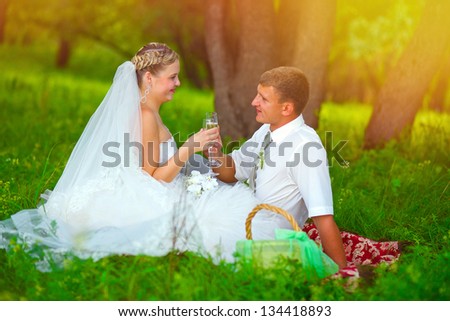 sunlight bride and groom at wedding in green forest sitting on picnic, drink wine from wine glasses at wedding