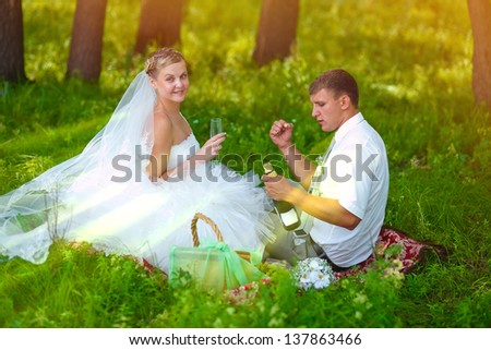 couple sunlight wedding newlyweds bride and groom a picnic in forest glade, groom opens champagne wine