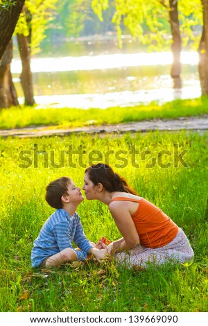 Mom and son woman and child sitting on grass kissing sunset Romantic