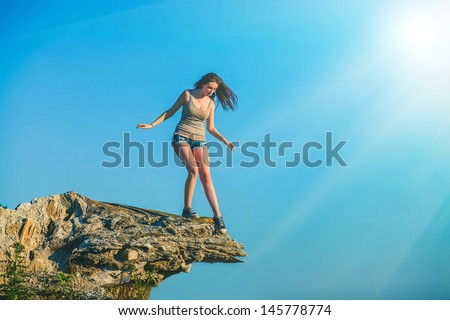 sunlight fear acrophobia woman tall stands on top of a rock cliff edge and is fearful horror