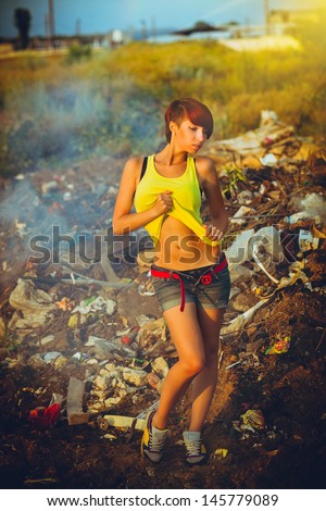 sunlight beautiful young fashion woman sexy punk homeless prostitute standing on a landfill in the smoke