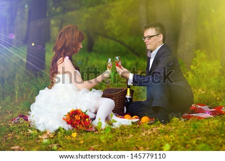sunlight Russia newlyweds couple bride, and groom sitting on green grass, picnic in woods at wedding drink wine