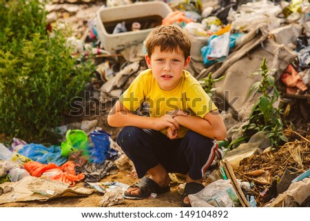 German homeless baby boy squatting on a rubbish dump in yellow t-shirt with tousled hair