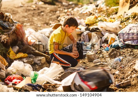 German homeless boy child blonde in yellow a jersey at garbage dump looking for food