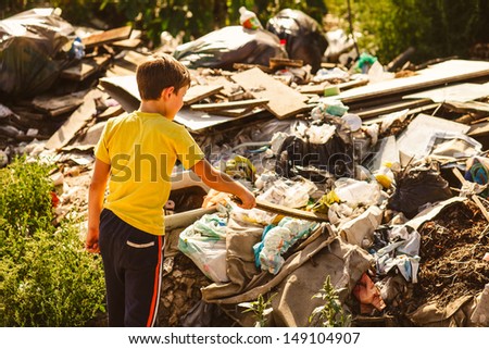 German homeless boy child blonde in yellow jersey a at garbage dump looking for food