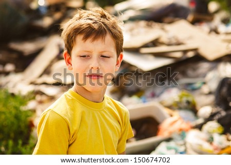 german homeless boy poverty child is a on garbage dump in a yellow T-shirt with her air disheveled poverty
