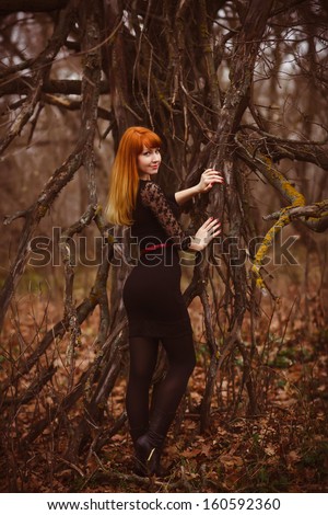 red-haired model woman girl in black dress dry autumn dark forest, dry branches on street
