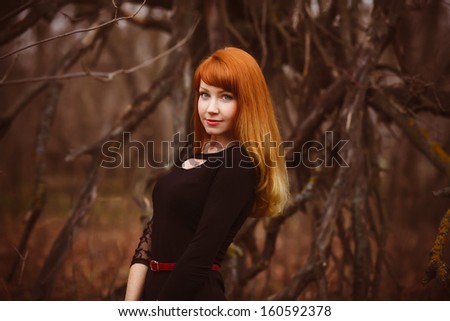 red-haired model face girl in black woman dress dry autumn dark forest, dry branches on street