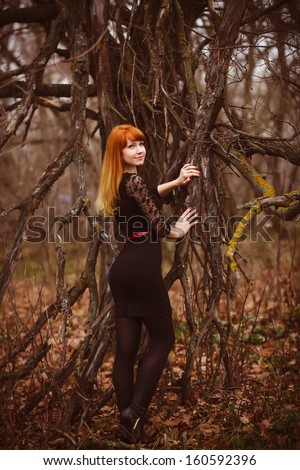 woman red-haired model girl in black dress dry autumn dark forest, dry branches on street