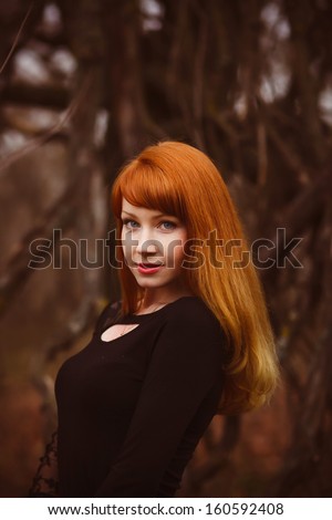 red-haired face model girl in black woman dress dry autumn dark forest, dry branches on street